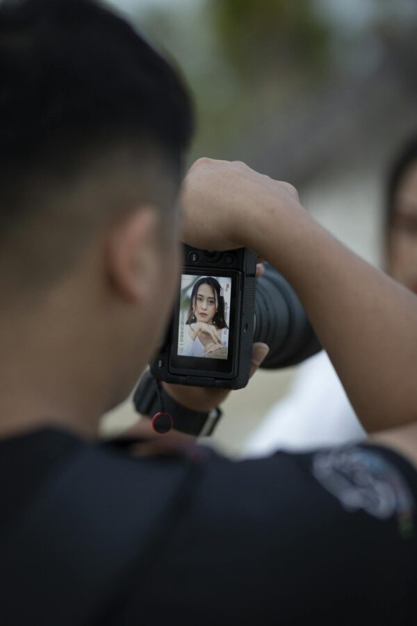 Photo by HONG SON Back view of crop unrecognizable male photographer taking shot of young ethnic female model during professional photo session in park